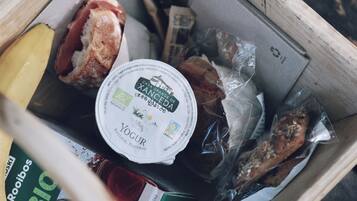Una caja de madera llena de diversos alimentos, como una barra de pan, un recipiente con yogur y aperitivos envasados.