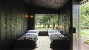 Una habitación con dos camas, paredes de madera y un ventanal con vistas a un bosque.