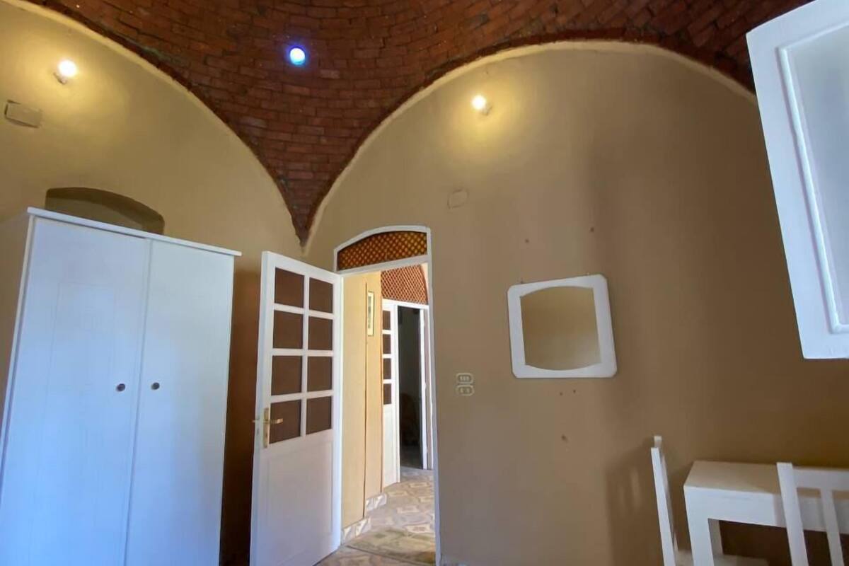 Ein Zimmer mit Ziegeldecke, einem Bett mit weißer Daunendecke, einem Schreibtisch und einem Stuhl.