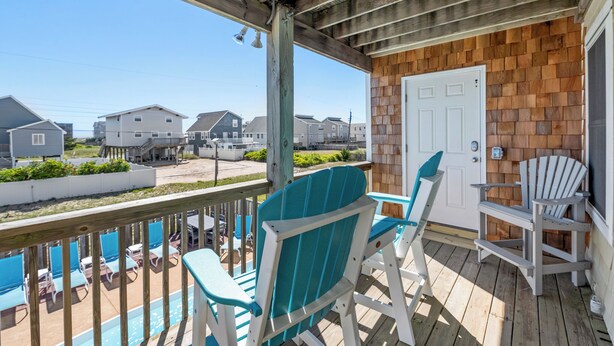 Une terrasse en bois avec des sièges extérieurs, une porte et une vue sur les maisons voisines.