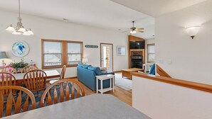 Un salon moderne avec un canapé bleu, une table à manger en bois et des chaises. On y trouve également un coin cuisine équipé d’une cuisinière et d’un ventilateur de plafond.