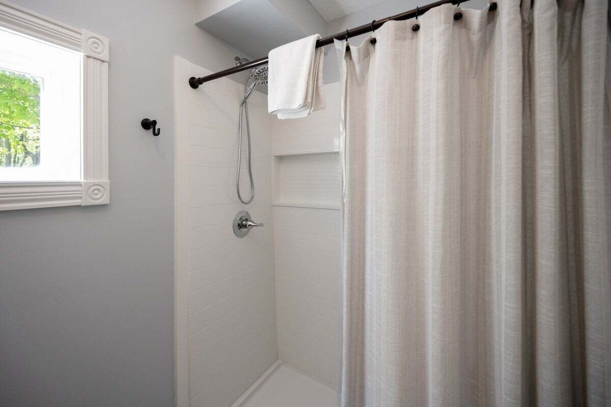 A shower with a glass door, a towel rack, and a window with a view of greenery.