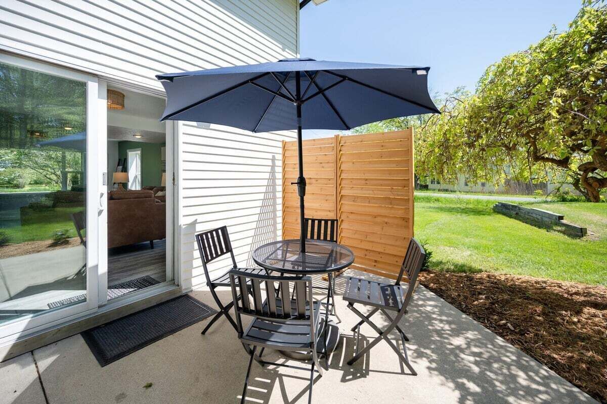 A patio with a round table and four chairs, a large umbrella, and a wooden fence.