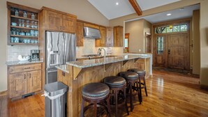 A kitchen with wooden cabinets, a stainless steel refrigerator, a granite countertop, and a bar area with stools. - Lake View Home with Access to Exclusive Golf (Bend)