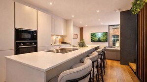 A modern kitchen with a large island, bar stools, a built-in oven, and a flat-screen TV.