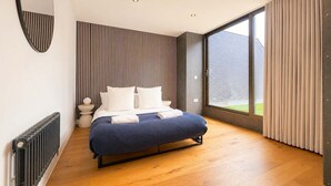 A modern bedroom with a large bed, a radiator, a round mirror, and a large window with curtains.