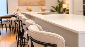 A modern kitchen with a bar area, bar stools, pendant lighting, and a large abstract painting on the wall.