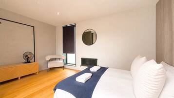 A modern bedroom with a bed, a chair, a radiator, and a wall-mounted mirror.