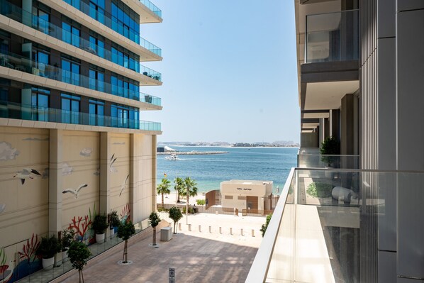 A modern building with multiple balconies overlooking a coastal area with a view of the sea and a sandy beach.
