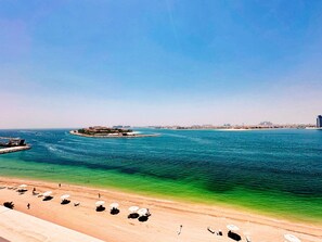 A beach with clear blue water, a sandy shore, and a few umbrellas.