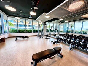 A gym with weightlifting equipment, benches, and a large window offering a view of greenery and buildings.