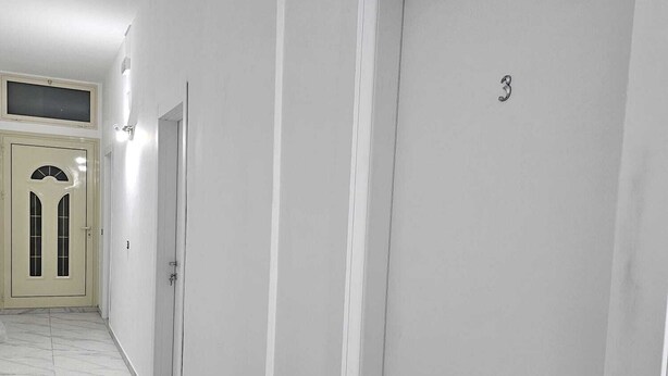 Un couloir aux murs blancs, doté d’un sol en marbre et de deux portes numérotées 3 et 4.