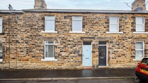 Une maison mitoyenne en pierre, dotée de nombreuses fenêtres, d’une porte et d’une antenne parabolique.