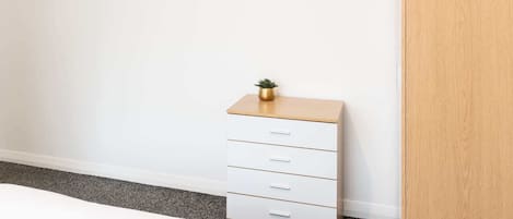 A bedroom with a bed, a white dresser with drawers, a small plant on top, and a wooden door.