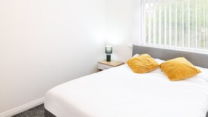 A hotel room with a bed, a nightstand, and a window with blinds. - Host & Stay | Broadway (Chadderton)