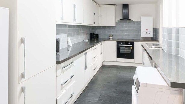 A modern kitchen with white cabinets, a black range hood, a built-in oven, and a coffee maker. - Host & Stay | Broadway (Chadderton)
