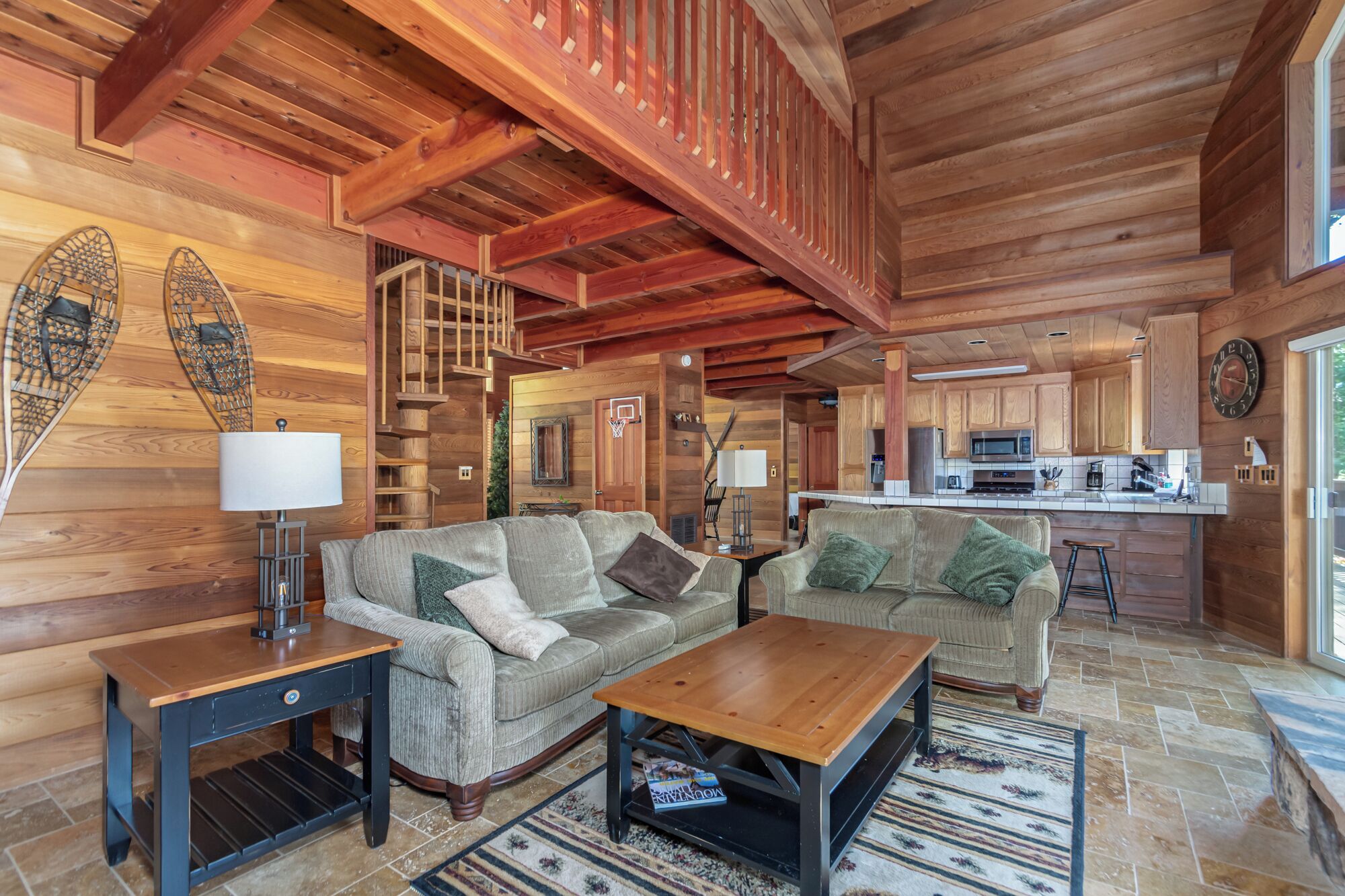 A cozy cabin interior with a living room, kitchen, and a wooden staircase.