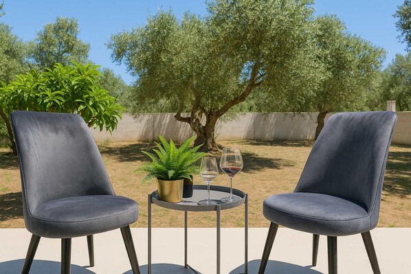 Deux fauteuils gris foncé, séparés par une petite table ronde, un pot de fleurs et deux verres à vin posés sur la table.
