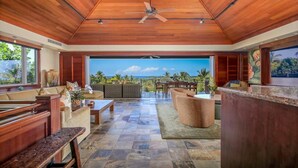 Un vaste espace de vie doté d’un plafond en bois, d’une grande fenêtre offrant une vue panoramique et d’un coin salon aménagé avec des canapés et une table basse.