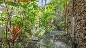 Un jardin tropical avec un sentier en pierre menant à un espace douche.