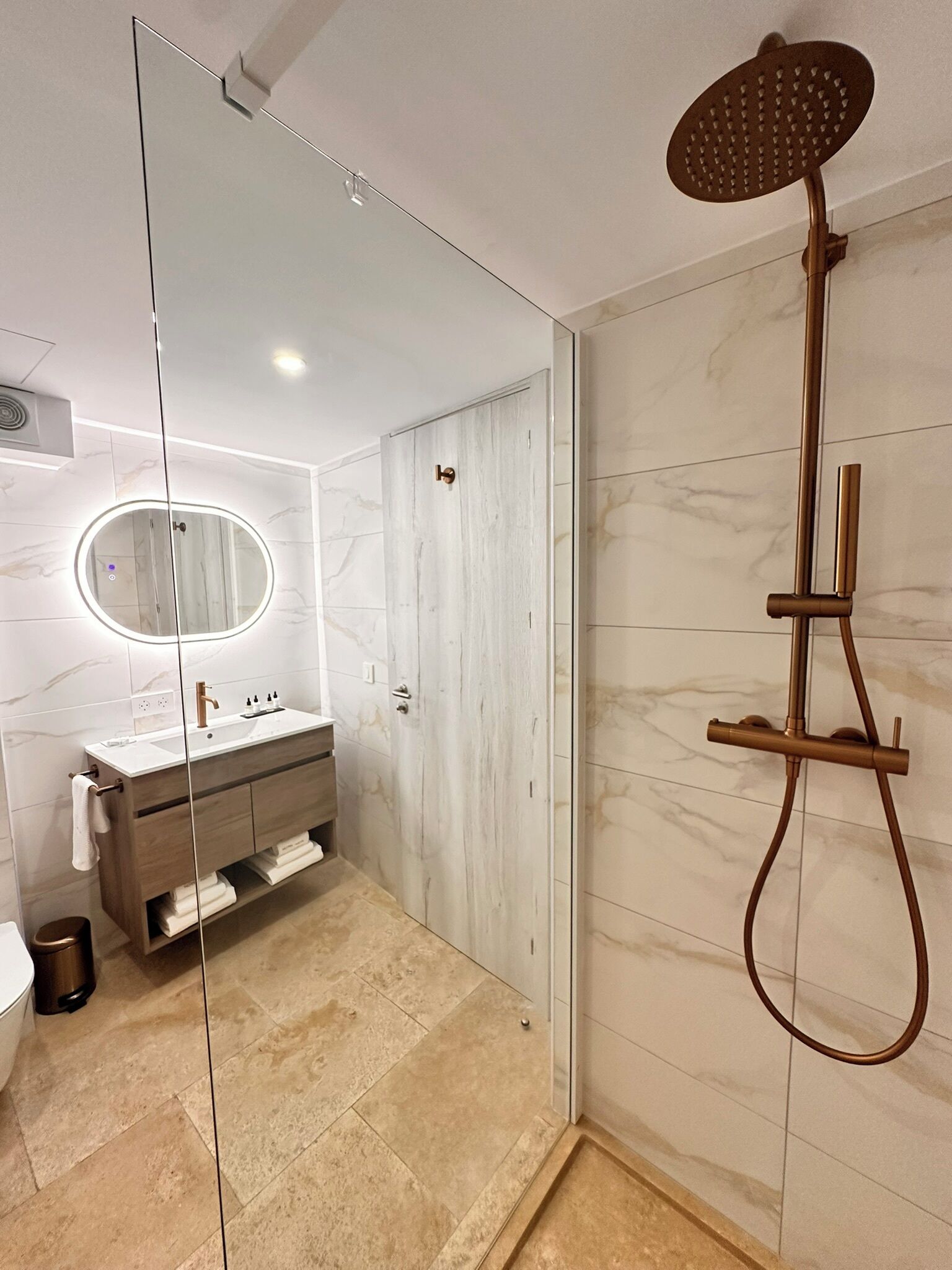 Un baño moderno con ducha de vidrio, tocador de mármol y un espejo grande.