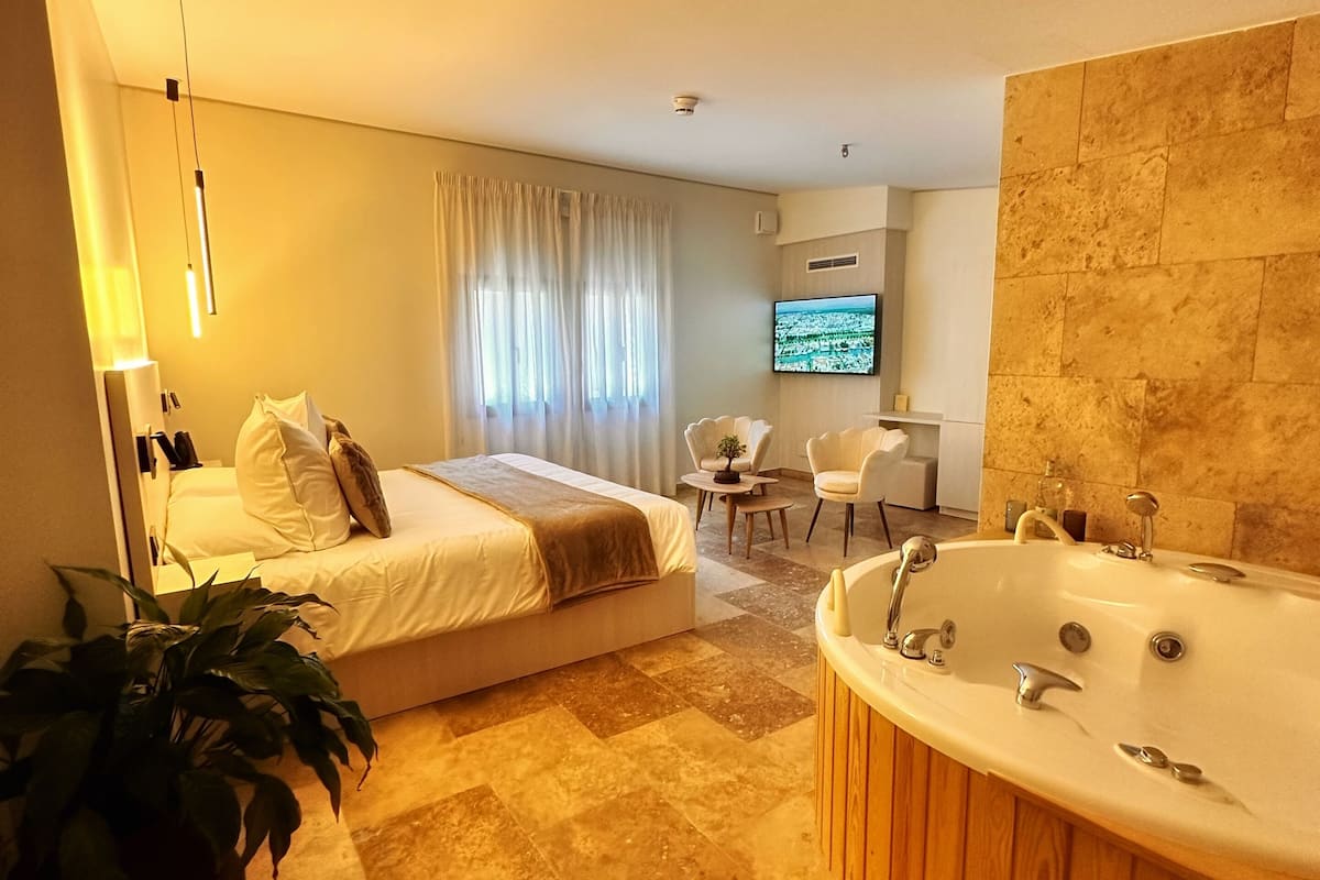 A modern hotel room with a large bed, a separate seating area, a TV, and a bathtub.