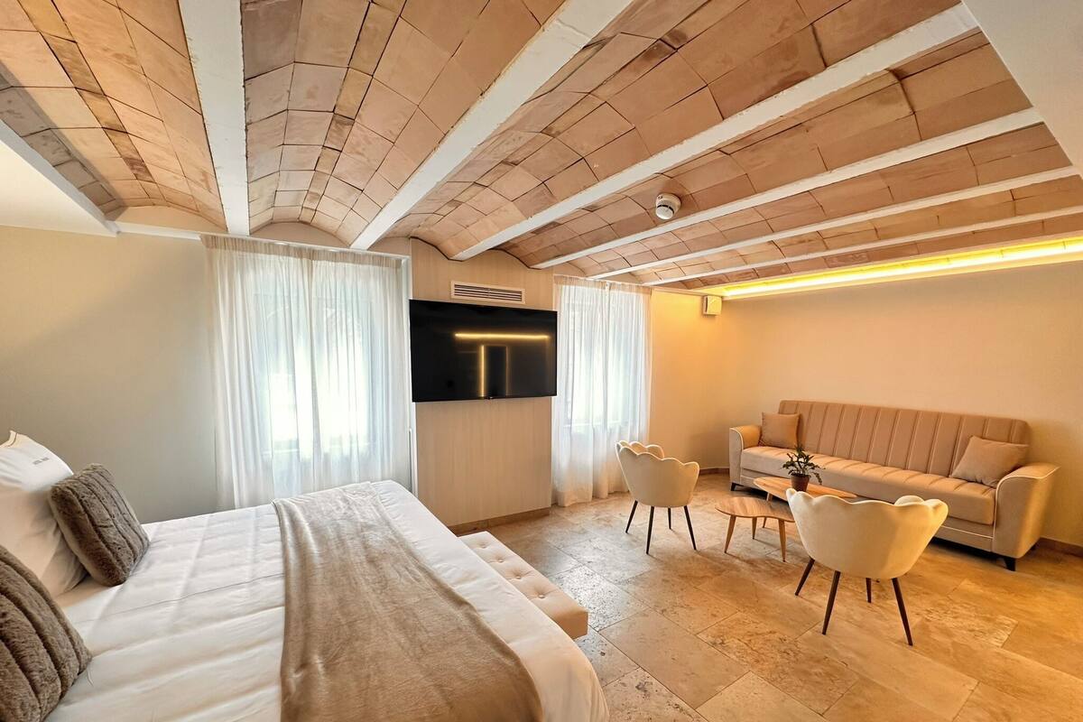 A modern hotel room with a large bed, a sofa, a TV, and a dining area.