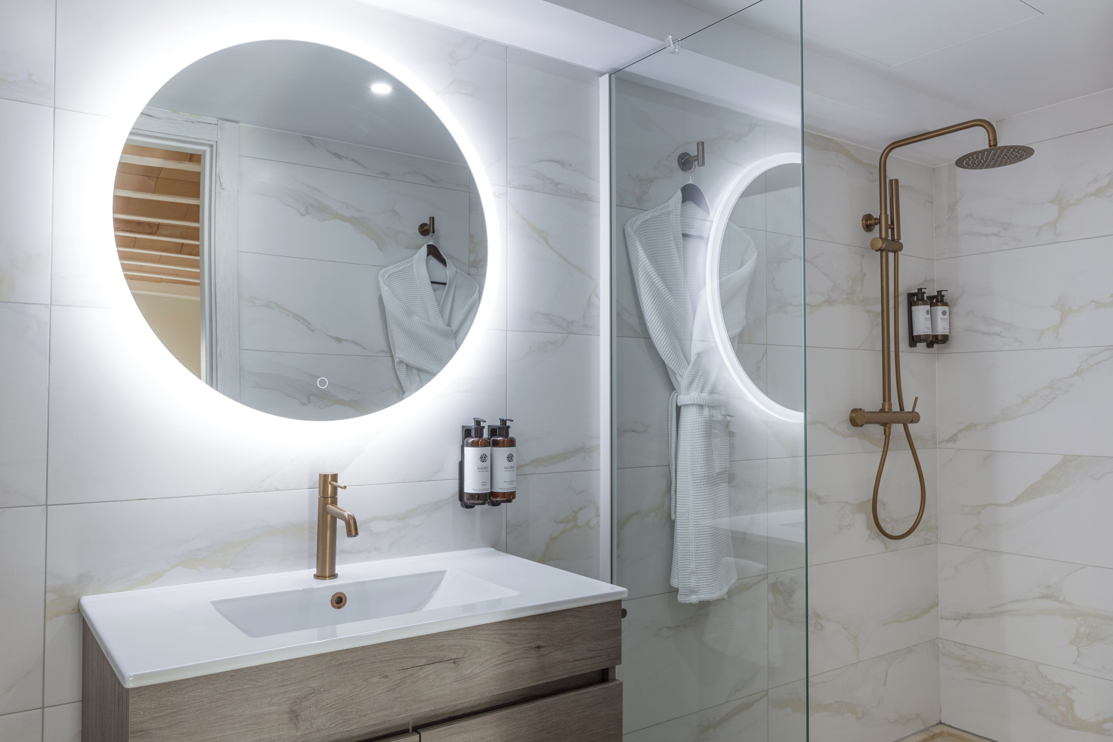 Un baño con espejo redondo, lavamanos y ducha.