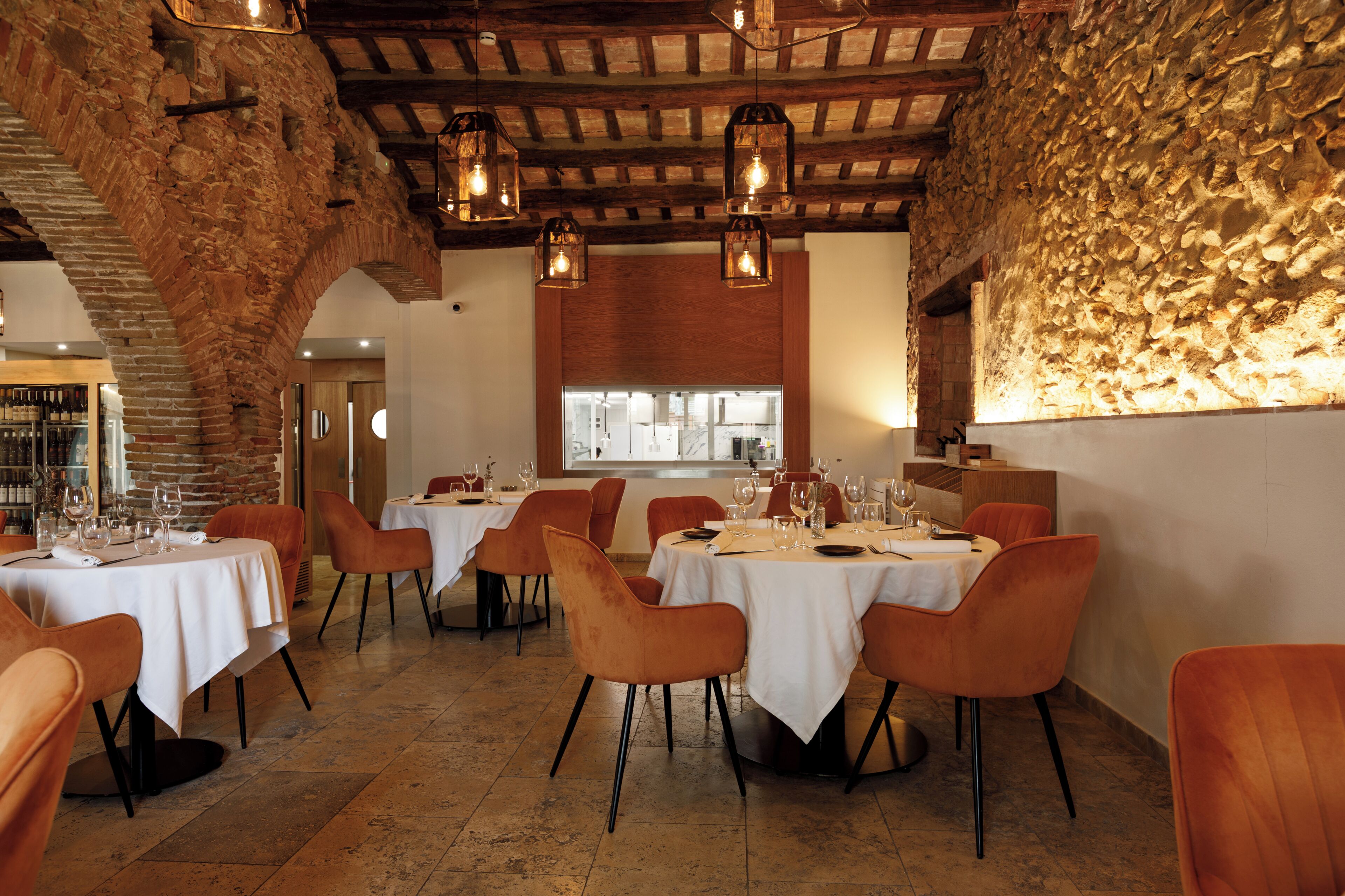 A restaurant with stone walls, wooden beams, and tables set for dining.