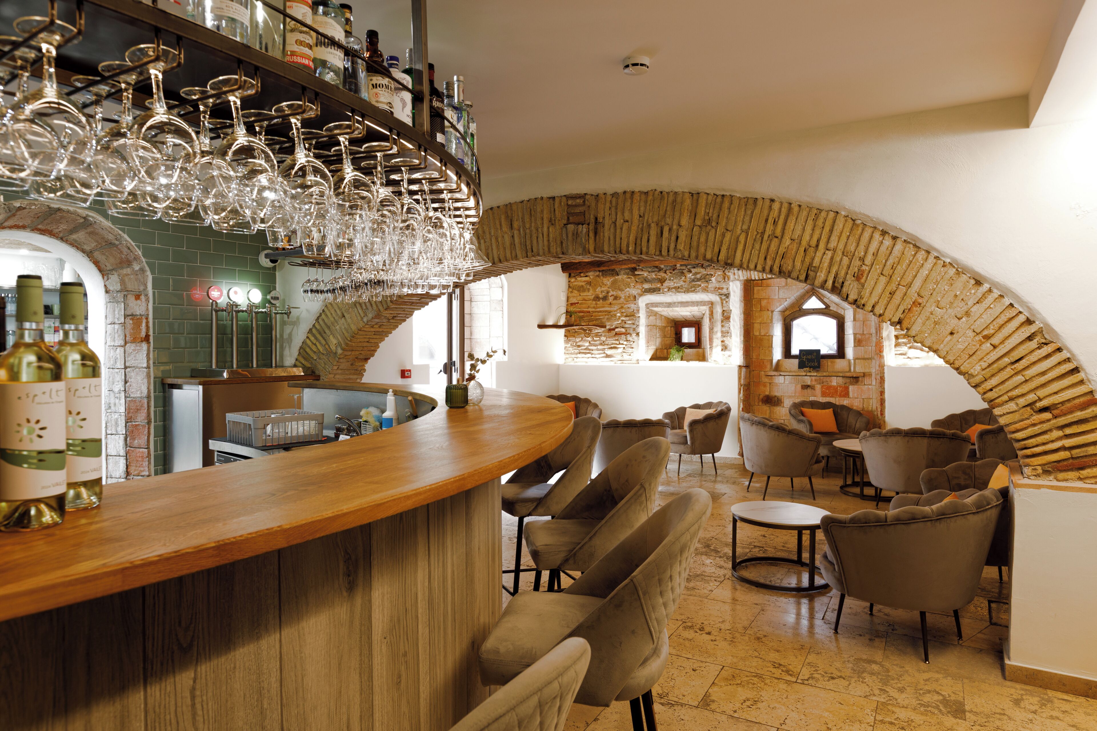 A bar area with a wooden counter, multiple wine glasses, and a brick archway.
