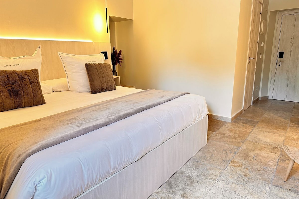 A hotel room with a large bed, a nightstand, and a door leading to another room.