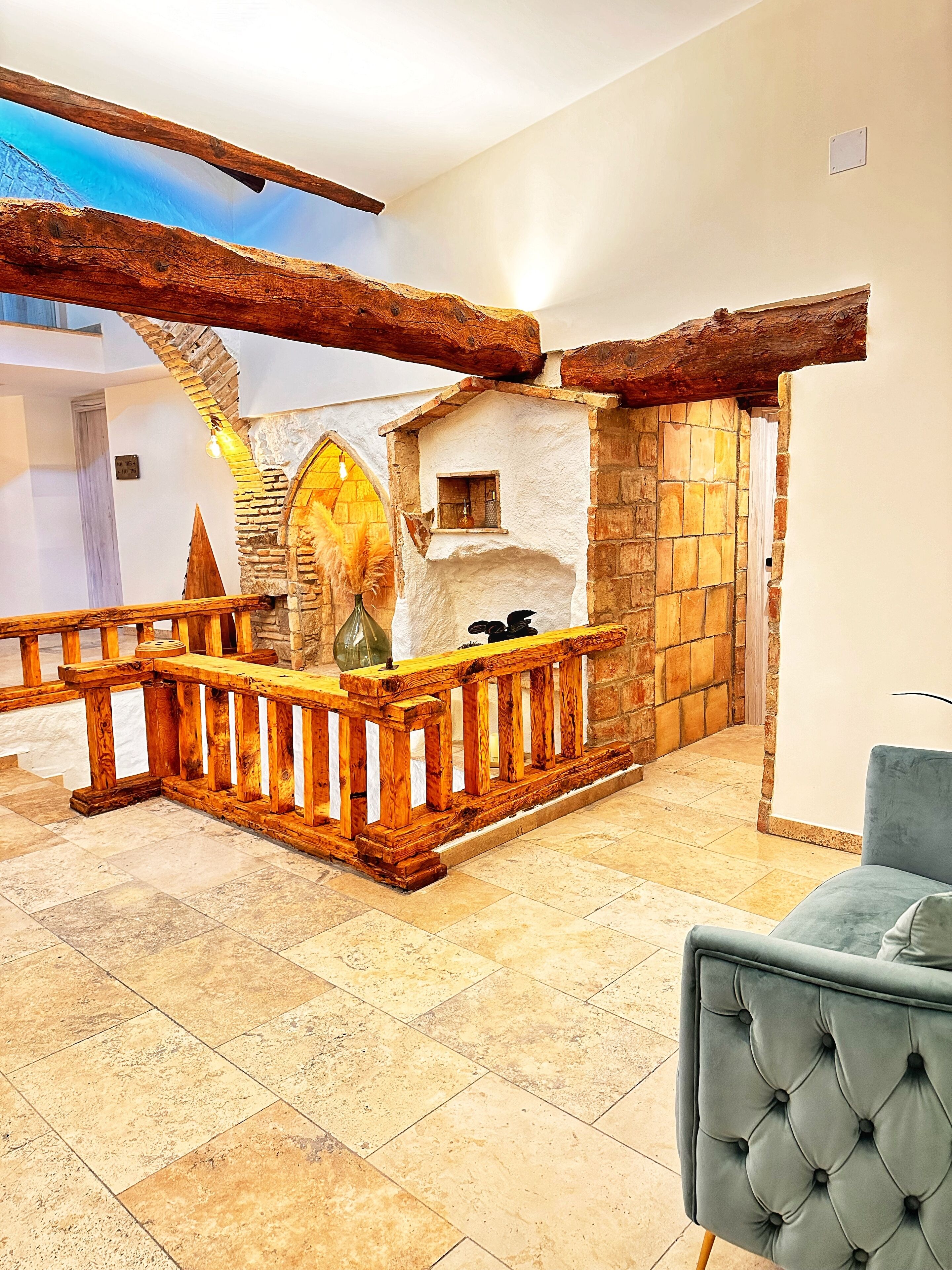Un interior moderno con chimenea de piedra, barandilla de madera y un sillón tapizado en azul.
