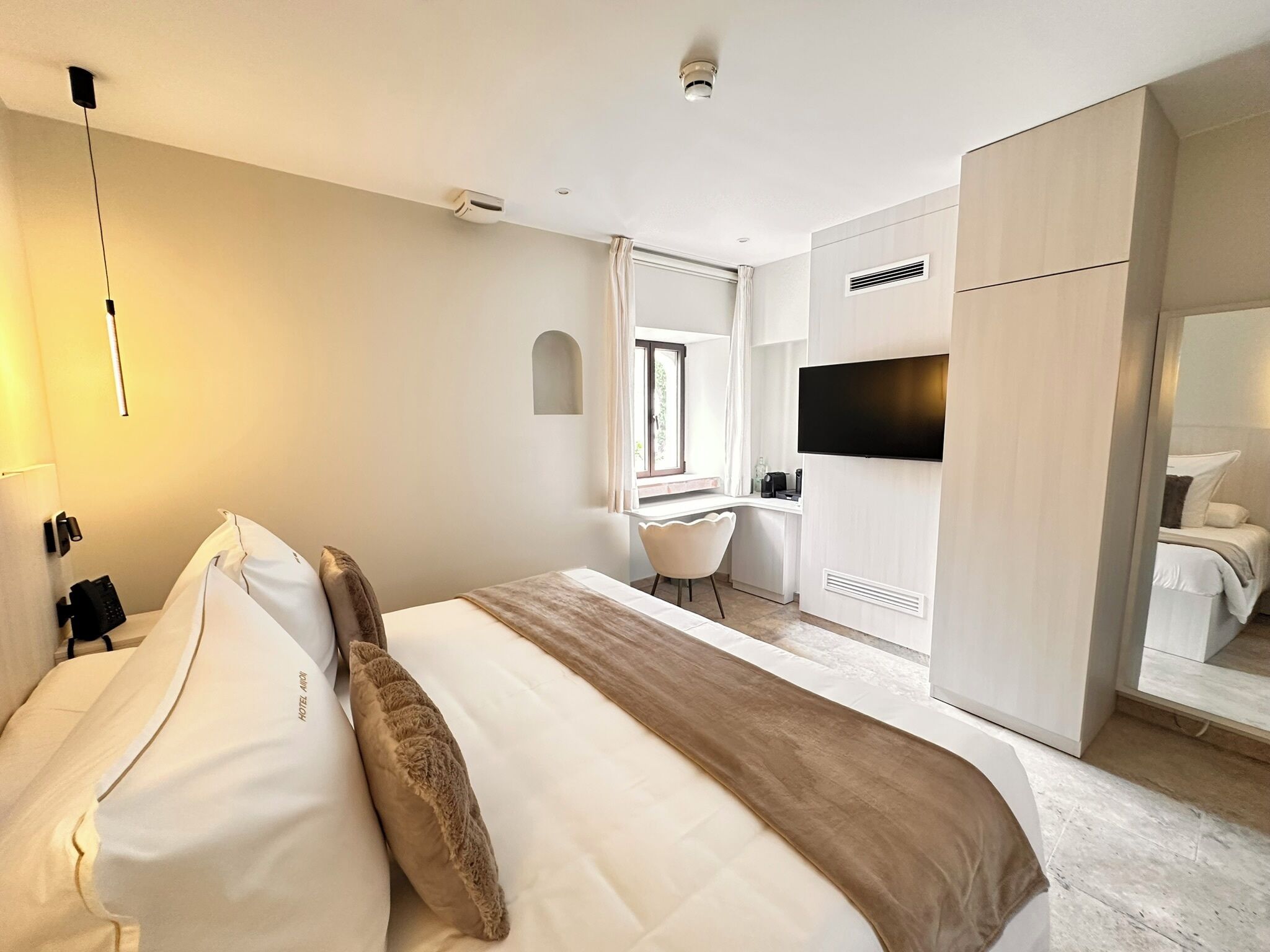 Una habitación de hotel con cama, escritorio, silla, televisor y armario.