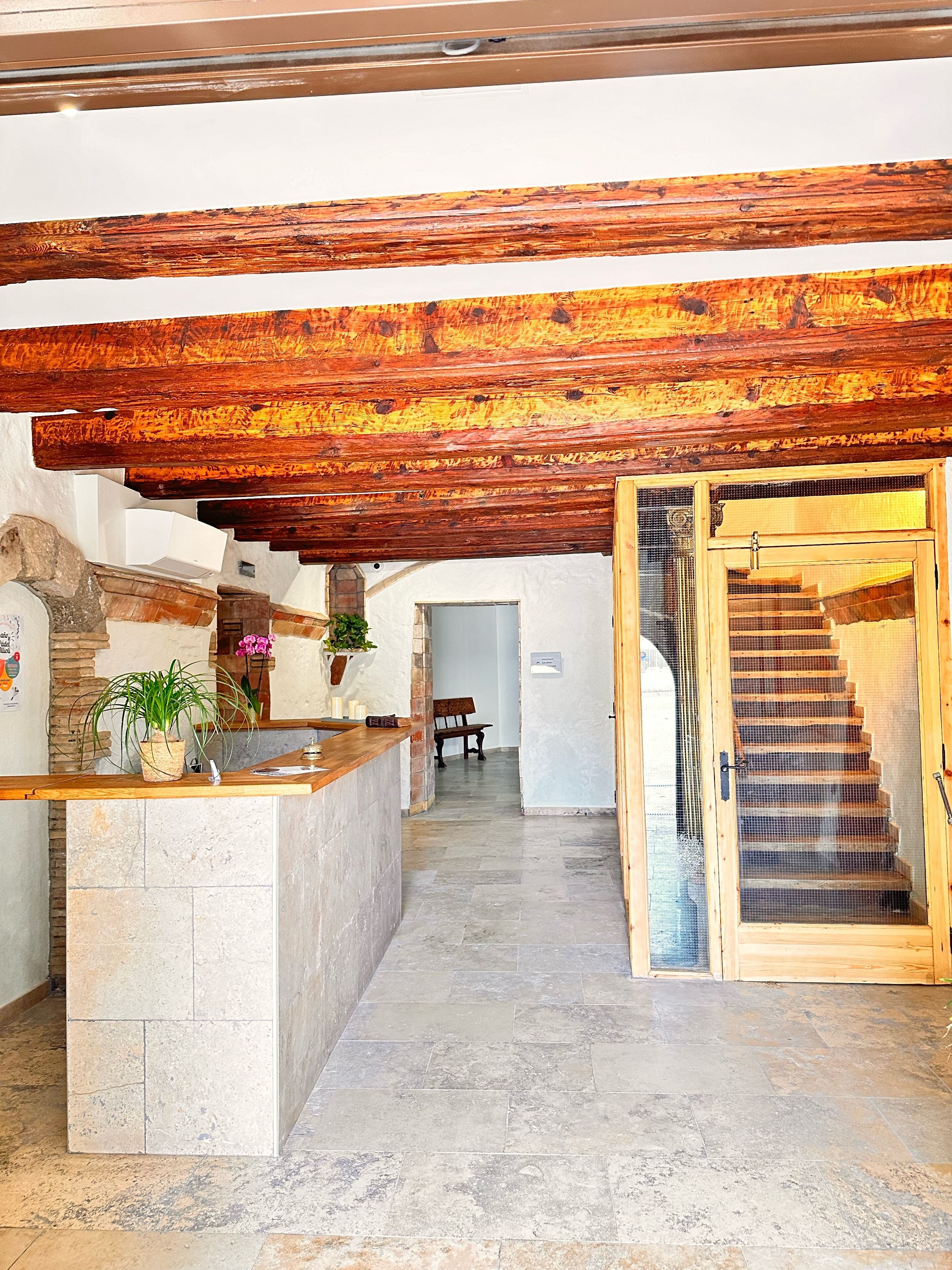 Una zona de recepción con mostrador de piedra, vigas de madera, una escalera y un banco.