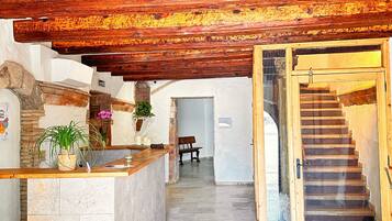 Una zona de recepción con mostrador de piedra, vigas de madera, una escalera y un banco.