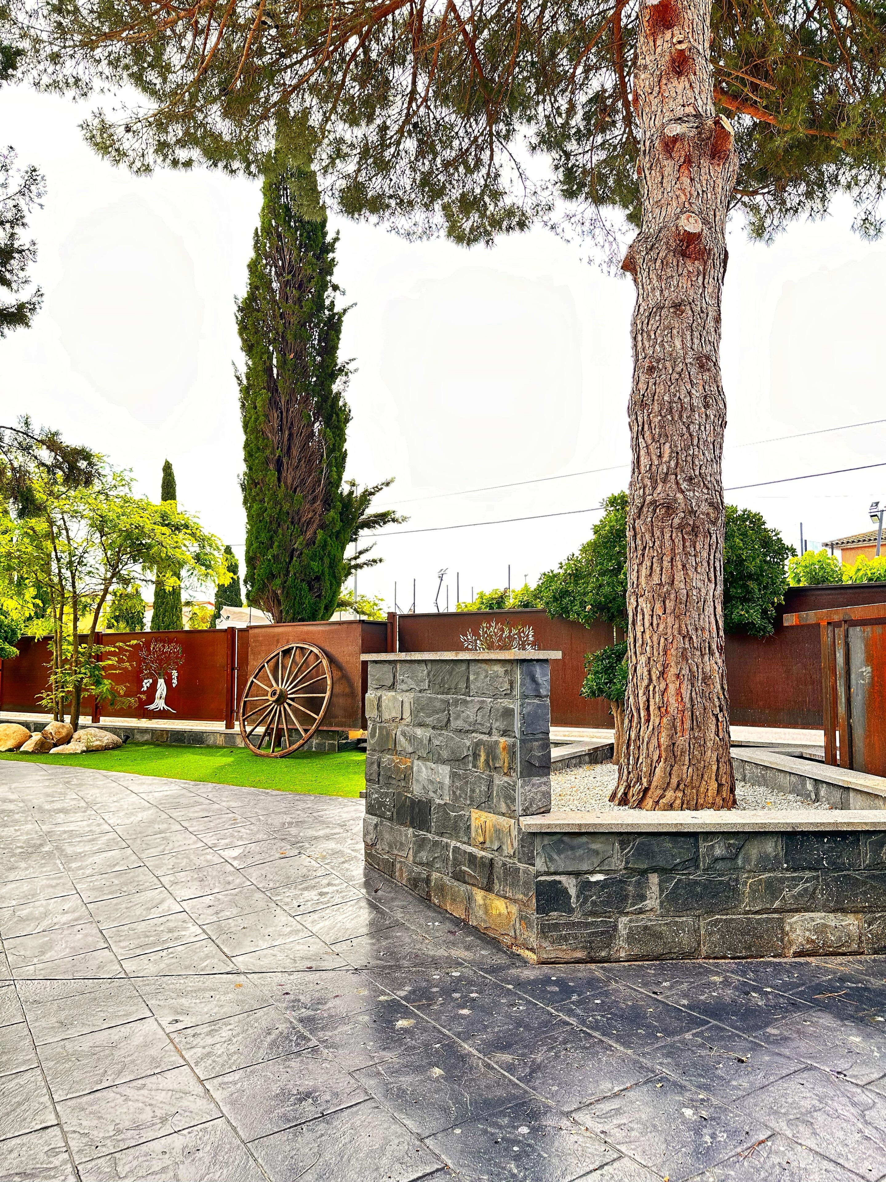 A courtyard with a stone planter, a large tree, and a decorative metal fence.