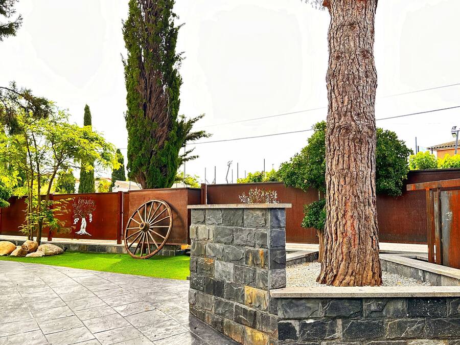 Un patio con una jardinera de piedra, un árbol grande y una valla decorativa de metal.