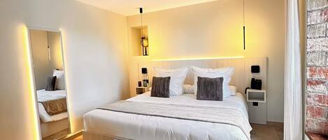 A modern bedroom with a large bed, bedside tables, a bench, and a mirror.