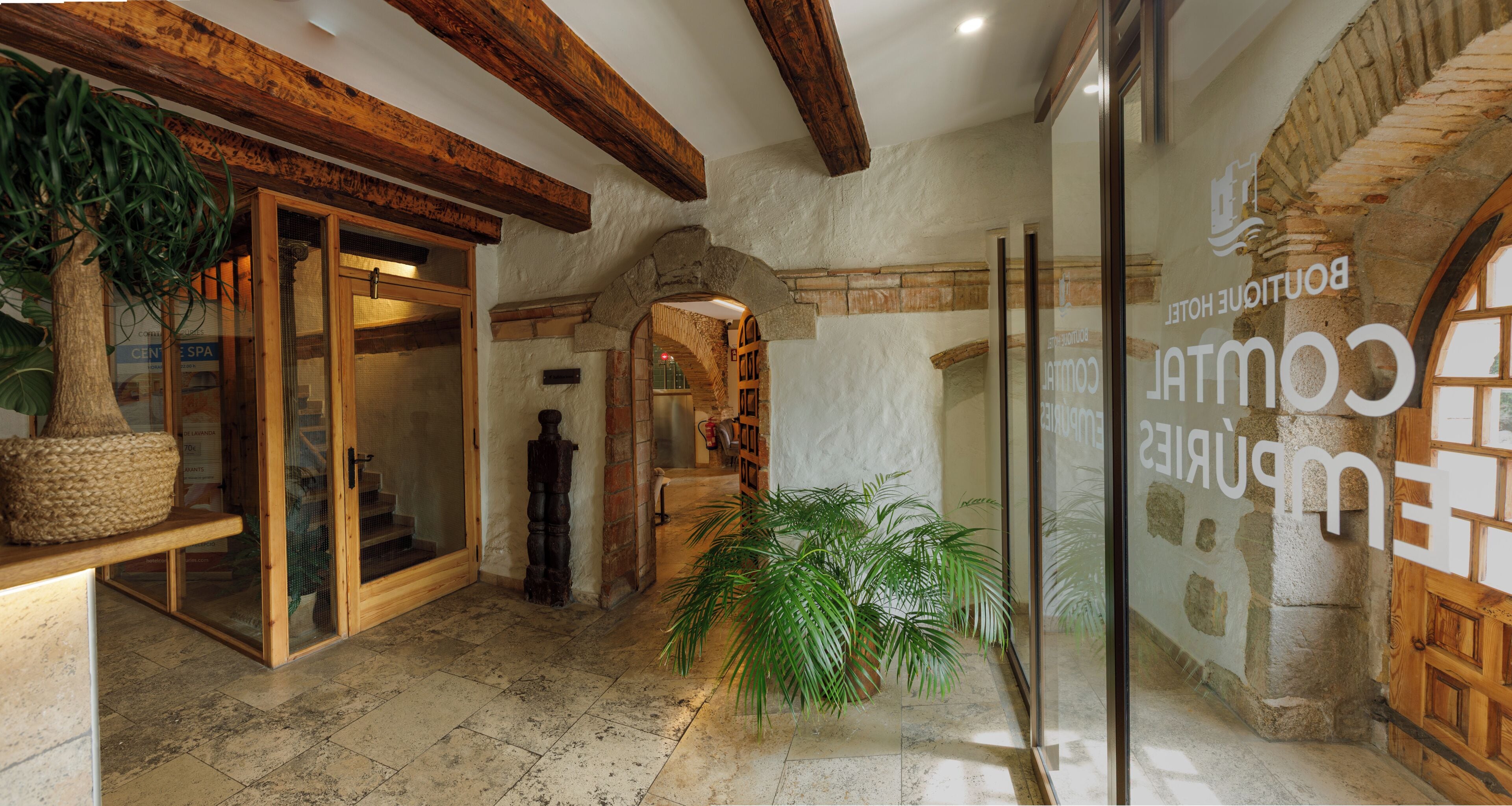 A hotel lobby with a stone wall, wooden beams, and a glass door leading to a spa area.