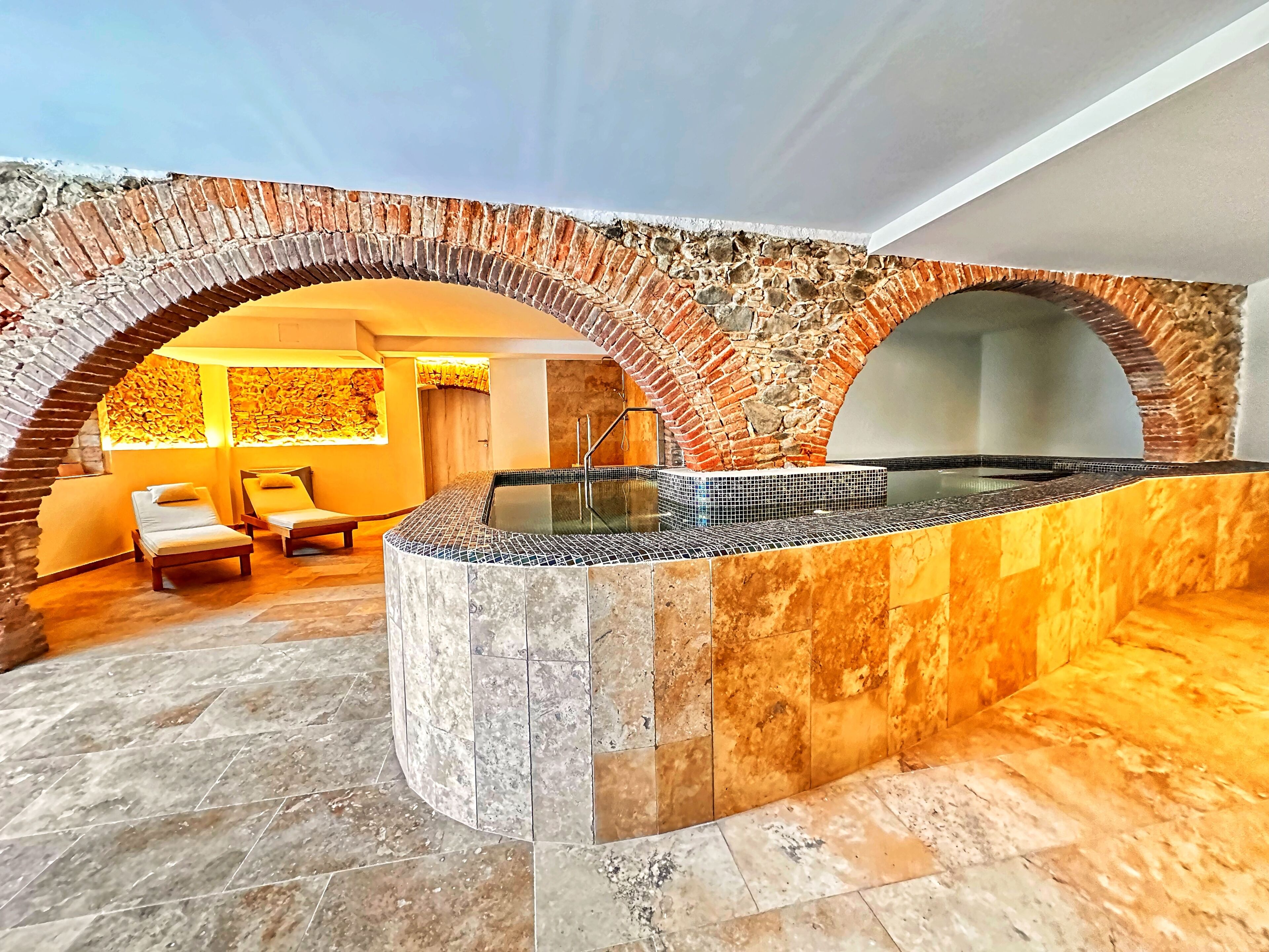 Een wellnessruimte met een stenen boog, een jacuzzi en comfortabele stoelen.