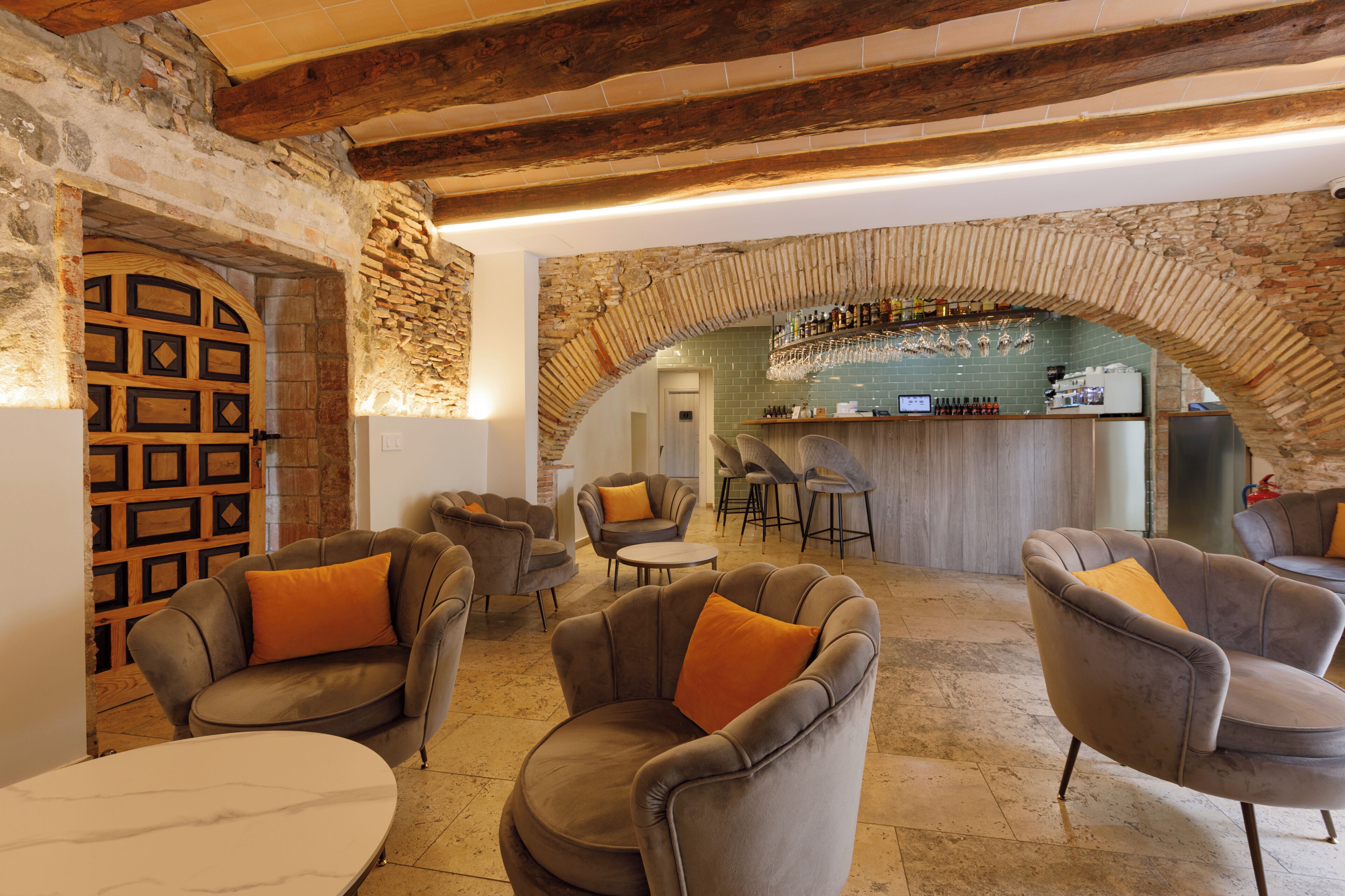 A bar area with stone arches, leather armchairs with orange cushions, and a bar counter with bottles.