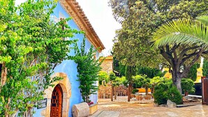 Un patio con un sendero de piedra, un edificio azul con una puerta de madera y un muro de piedra.