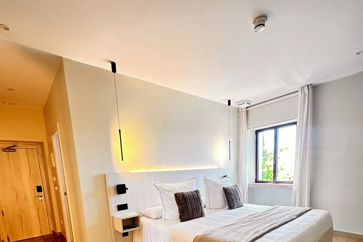 A modern bedroom with a large bed, a bedside table, a chair, and a window with curtains.