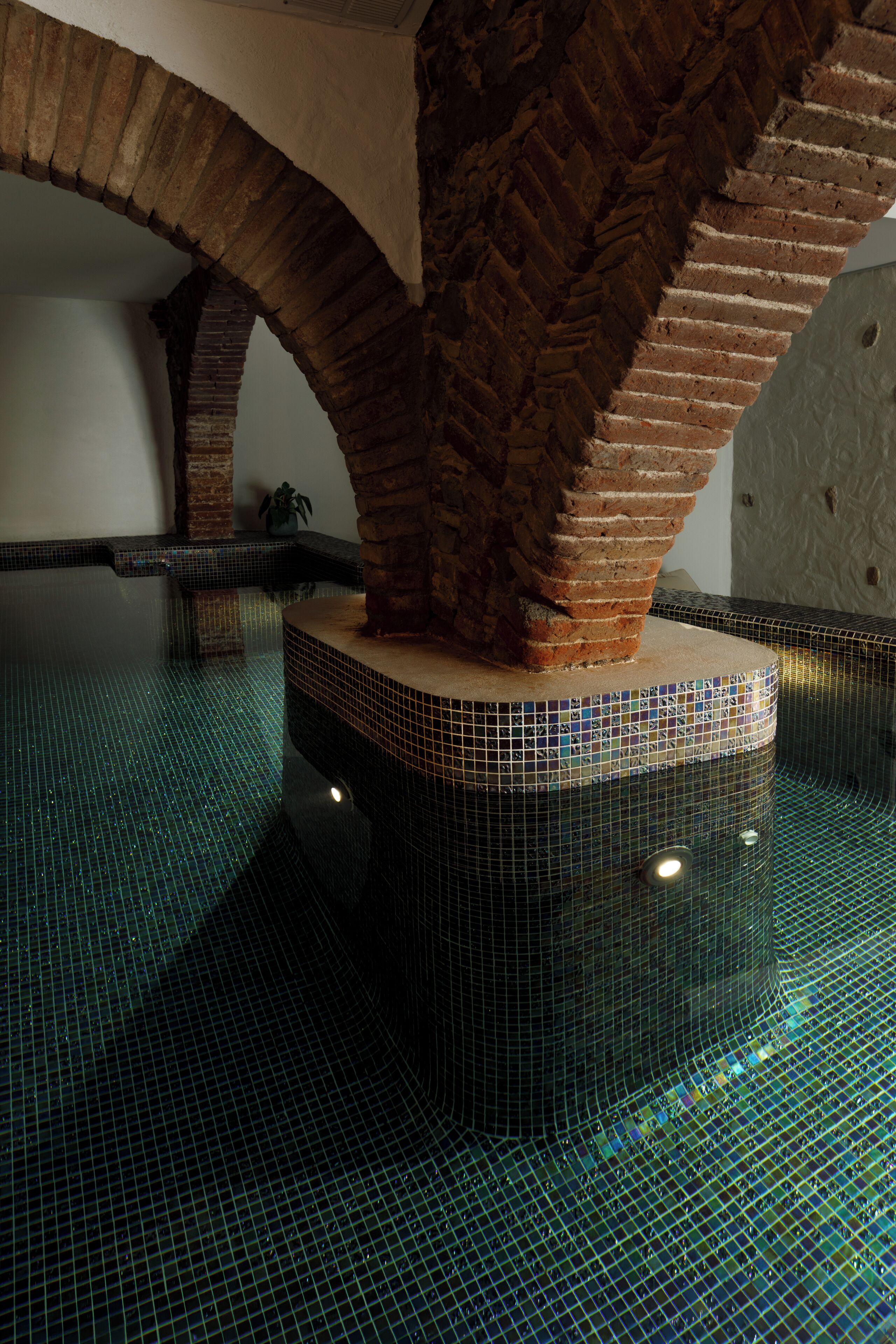 Una piscina con piso de baldosas y arcos de ladrillo.