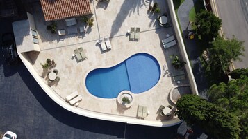 Vista aérea de una piscina con sillones de descanso y un pequeño jardín.