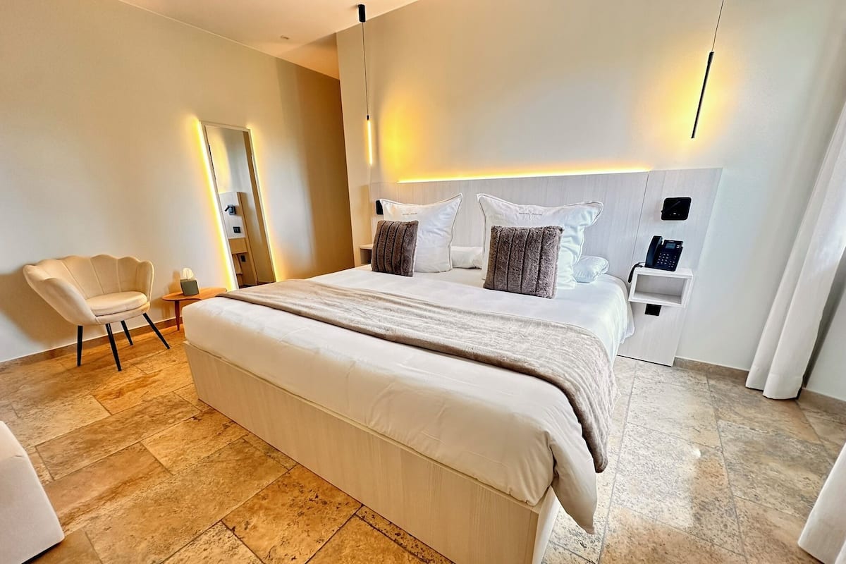 A modern hotel room with a large bed, a seating area with a chair, and a bedside table with a phone.