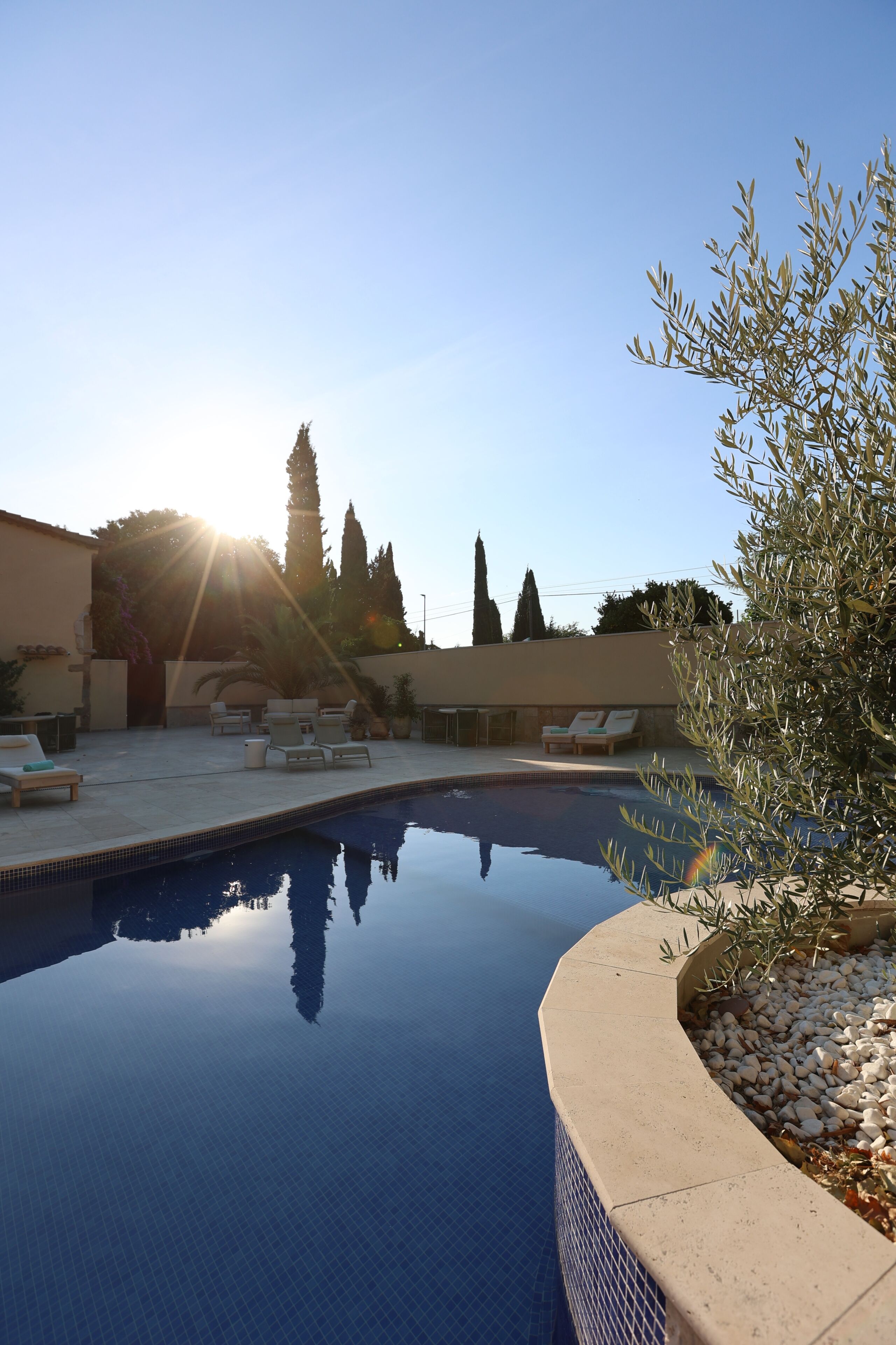 A swimming pool with lounge chairs and a pergola, surrounded by trees and a building.