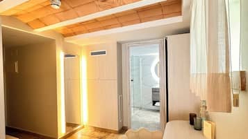 A modern interior with a wooden ceiling, a round table, and a chair. There is a hallway leading to a bathroom with a glass door.