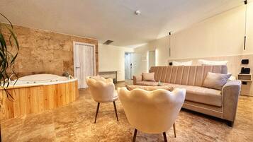 A modern bathroom with a bathtub, two chairs, and a beige sofa in a spacious living area.