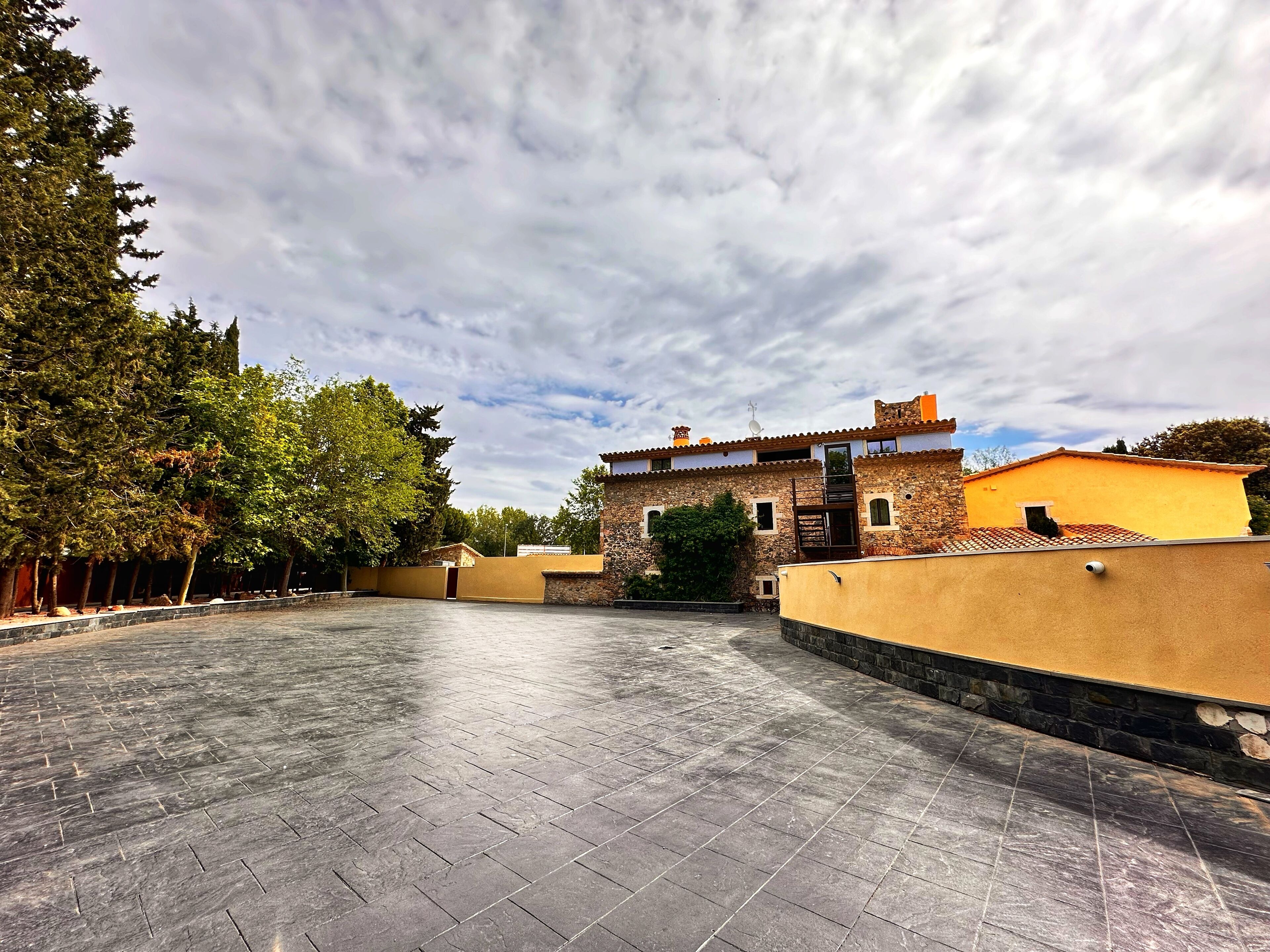 A courtyard with a stone wall, a building with a tiled roof, and trees.